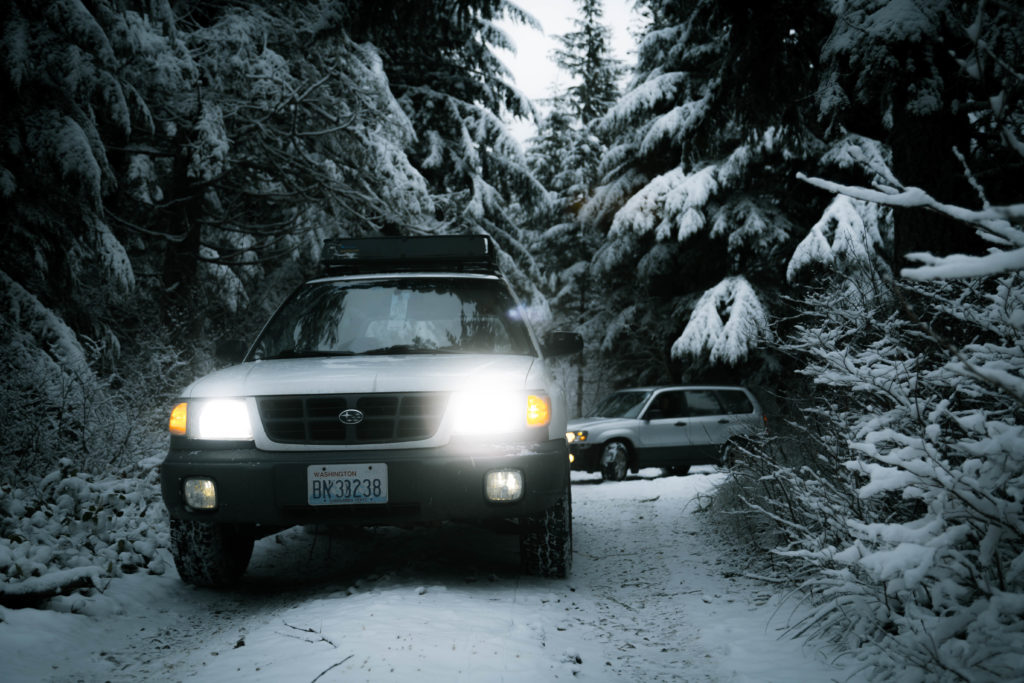 subaru forester in the snow with bright headlights, toyo open country all terrain tires and a lift kit
