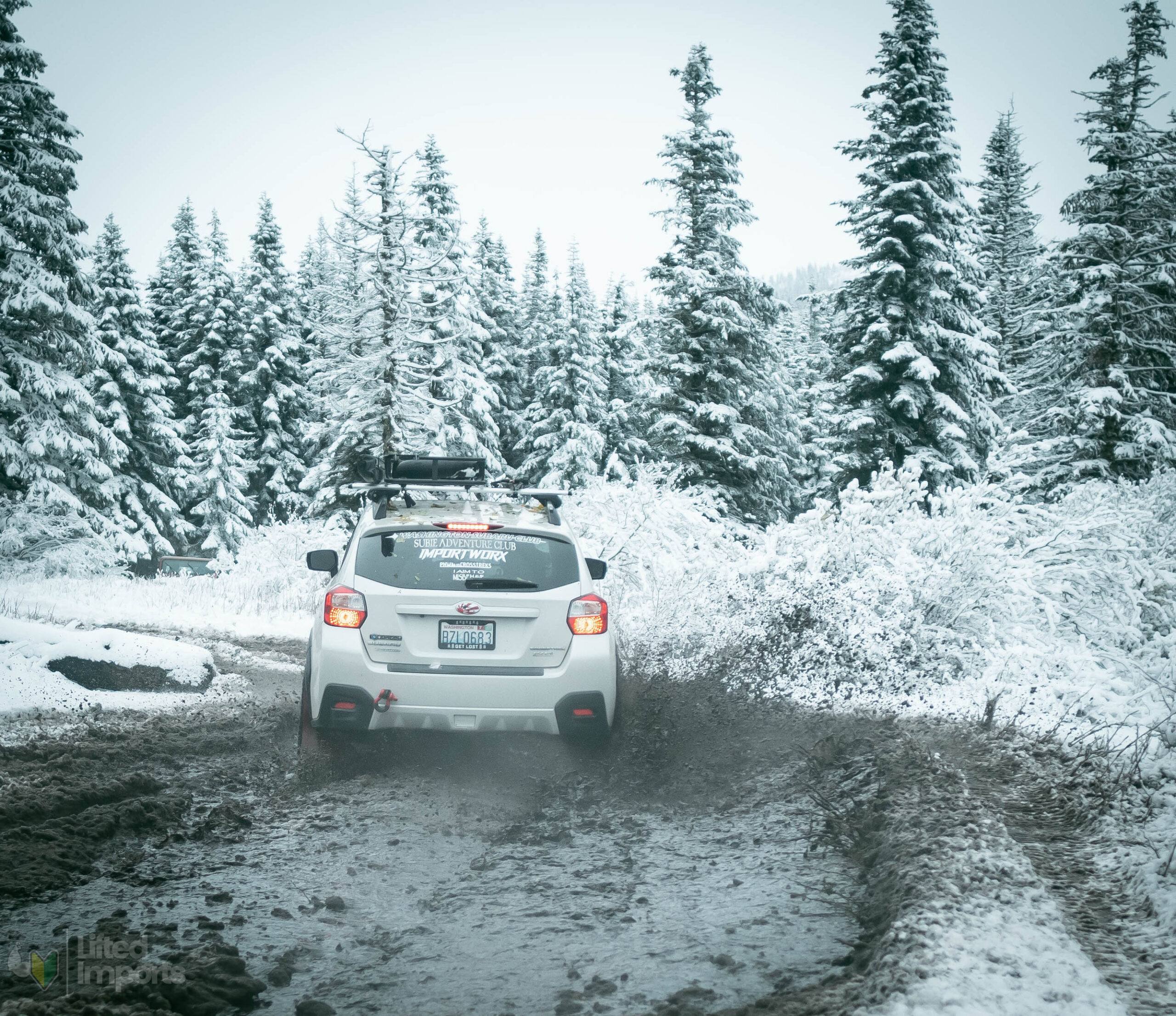 white lifted subaru crosstrek with offroad tires and method mr502 wheels in the snow going through mud back shot