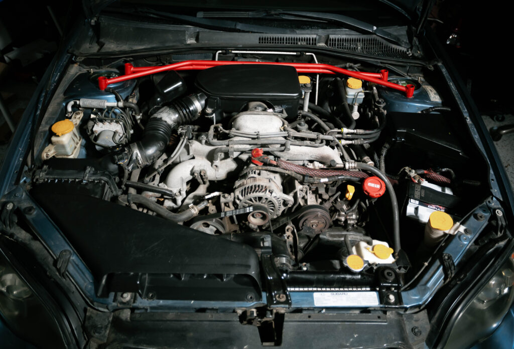 engine bay of a subaru with a strut tower brace and upgraded battery