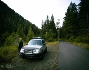 man standing next to 2006 lifted subaru forester in the woods
